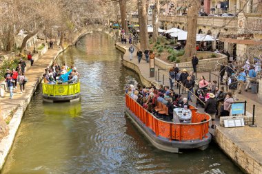 San Antonio, Teksas, ABD - Şubat 2023: Nehir teknelerinde şehir merkezinden geçen ziyaretçilerin hava görüntüsü
