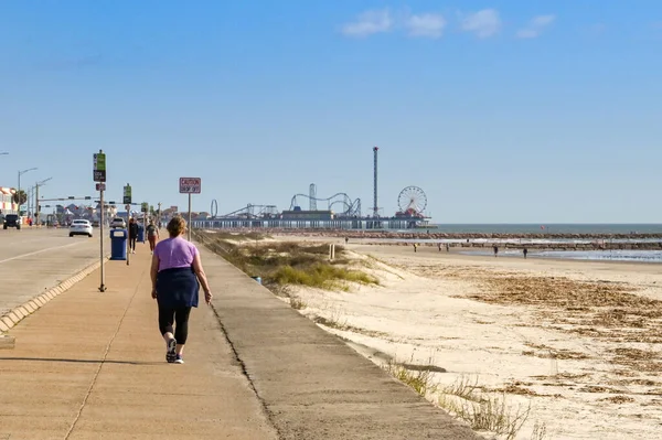 Galveston, Teksas, ABD - Şubat 2023: Arka planda kentin tarihi iskelesi boyunca yürüyen kişi