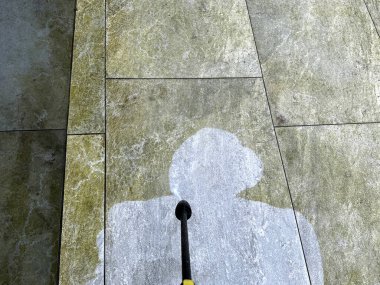 High pressure jet washing equipment being used to clean porcelain tiles on a garden patio, with contrast between the parts before and after cleaning. No people. clipart