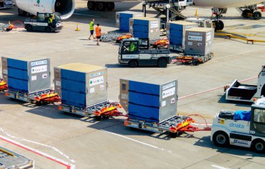 Londra, İngiltere, İngiltere - 14 Haziran 2023: Heathrow havaalanındaki terminallerden birinde yük arabalarının önünde çekilen hava taşıma paletleri.