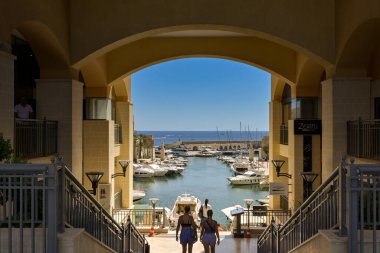 St Julians, Malta - 2 Ağustos 2023: İnsanlar marinada tekne ve yatlarla Pordomates geliştirme binasına doğru yürüyorlar.