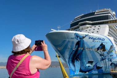 Manzallio, Mexicivo - 16 Ocak 2024: Seyahat gemisi yolcusu cep telefonuyla Norveç Saadet Gemisi 'nin fotoğrafını çekiyor