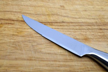 Keskin paslanmaz çelik bıçak, tırtıklı kenarı olan tahta bir tahtanın üzerinde önceki kesiklerin çizgileriyle işaretlenmiş.