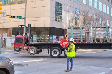 Austin, Teksas, ABD - 8 Şubat 2023: İnşaat işçisi, büyük eklemli bir kamyon inşaat sahasına girerken trafiği durdurmak için dur levhasını kaldırdı