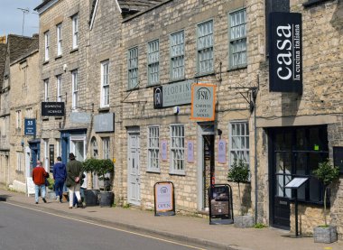 Tetbury, Gloucestershire, England, UK - 13 April 2024: People walking past shops ansd restaurants in the centre of the historic rural town of tetbury. clipart