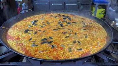 Büyük yuvarlak paella tavası pişerken köpürüyor. 