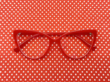 Pair of red cat eye shape women's glasses on a red polka dot background. Eye health concept. clipart