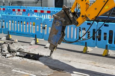 Londra, İngiltere, İngiltere - 21 Haziran 2022: Pnömatik matkap eklentisine sahip Excavaor, Londra şehir merkezindeki bir caddenin yol yüzeyini boru döşemek için kullanılıyor.
