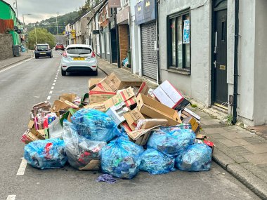 Treforest, Pontypridd, Wales - 5 September 2024: Cardboard boxes and plastic bags of sorted rubbish for recycling on the street outside a take away foor shop for the weekly collection clipart