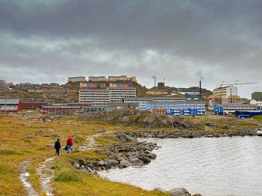 Qaqortoq, Greenland - 28 August 2024: People walking alongside the edge of Lake Tasersuaq with the town in background. clipart