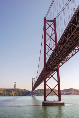 25 de Abril Köprüsü asma köprüsünün Lizbon 'daki Tagus Nehri üzerindeki manzarası. Arka planda İsa' nın Sığınağı olan Kral heykeli var.