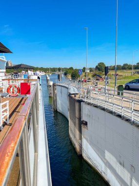 Veere, Seeland, The Netherlands - 10 August 2022: River cruise ship entering in the canal lock in the town of Veere with a narrow gap between the ship and the wall. clipart