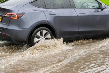 Treforest Industrial Estate, Wales, UK - 24 November 2024: Car driving through floodwater from the River Taff after it burst its banks after heavy rain clipart