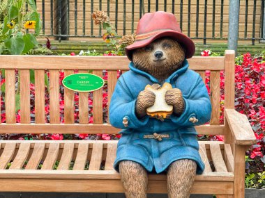 Cardiff, Wales - 10 Kasım 2024: Cardiff şehir merkezindeki halka açık bir parktaki ahşap bir bankta oturan Paddington Bear mankeni