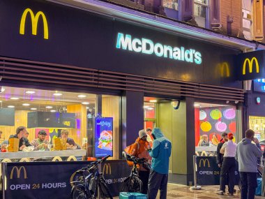 Cardiff, Wales, UK - 17 November 2024: Delivery riders waiting for orders outside a branch of McDonalds in the city centre at night clipart