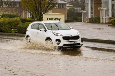 Treforest Industrial Estate, Wales, UK - 24 November 2024: Car driving the water on a flooded road on Treforest industrial estate after heavy rain from Storm Bert. clipart