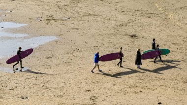 Bude, Cornwall, İngiltere, İngiltere - 22 Şubat 2025: Bude sahilinde sörf tahtaları taşıyan insanların hava görüntüsü