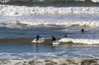 Bude, Cornwall, İngiltere, İngiltere - 22 Şubat 2025: Bude sahilindeki sahil beldesinde sörf yapan insanlar