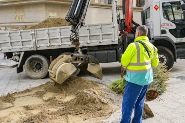 Vigo, İspanya - 14 Ocak 2025: Uzaktan kumandalı hidrolik vinç ve kova ile şehir merkezindeki yayaların oluşturduğu sokaktan toprak ve moloz toplayan bir kamyon şoförü