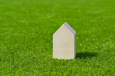 Small wooden model house isolated on the lush green grass of a lawn. Housebuilding and home ownership concept. Copy space.