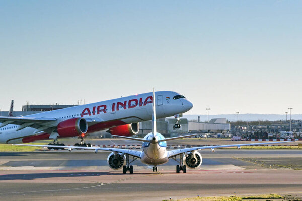 London, England, UK - 3 January 2025: Small passenger jet waiting to cross one of the runways at London heathrow Airport while an Air India Airbus A350 takes off.