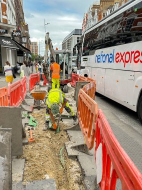 Londra, İngiltere, İngiltere - 27 Haziran 2023: Londra 'nın merkezindeki kaldırımda hendek kazan adam güvenlik bariyerinin diğer tarafından geçen trafik.