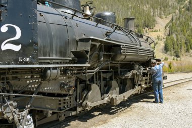 Silverton, Colorado, ABD - 23 Mayıs 2025: Durango ve Silverton dar göstergeli demiryolu üzerinde eski bir buhar makinesinin tekerleklerini yağlayan tren mühendisi