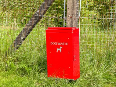 Publlic parkındaki çite bağlanmış köpek atıkları için kırmızı metal çöp kutusu. Kimse yok..