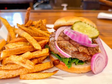 Lezzetli bir hamburgerin yakın görüntüsü. Patates kızartması, soğan ve turşulu taze çörek.