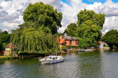 Marlow, Buckinghamshire, İngiltere, İngiltere - 20 Temmuz 2025: Marlow 'daki Thames Nehri' nin kıyısındaki evlerin yanından geçen bir motorlu tekne manzarası.