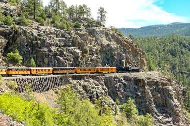 Durango, Colorado, ABD - 23 Mayıs 2025: Durango ve Silverton dar ölçü demiryolundaki buharlı motor kayalık bir dağın çıkıntısı etrafında bir tren dolusu koçu çekiyor