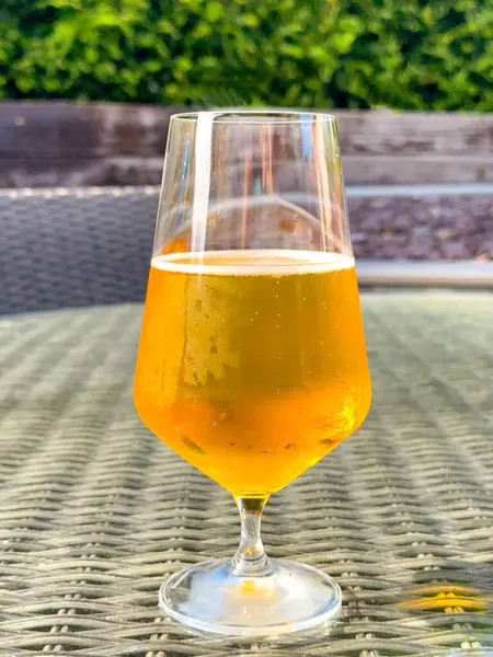 Bir evin arka bahçesindeki masada duran bir bardak altın bira. Kimse yok..