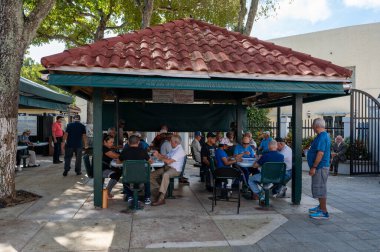 Miami, Florida - 11-26-2022 - Turistler ve Kübalı yaşlılar güneşli bir sonbahar öğleden sonrasında Küçük Havana 'da Calle Ocho' daki Domino Park 'ta kaynaşıyorlar..