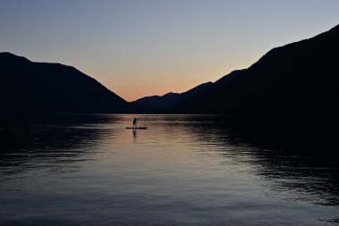 Washington Olimpiyat Ulusal Parkı 'ndaki Crescent Gölü' nde gün batımında siluet içinde kürek çeken kadın raket..