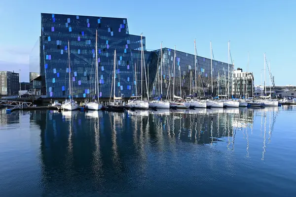 Reykjavik, İzlanda - 4 Eylül 2023 - Harpa Konser Salonu ve marina güneşli bir sonbahar sabahı Reykjavik Limanı 'nın sakin sularına yansıdı.