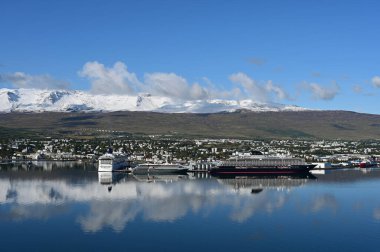 Akureyri, İzlanda - 9 Eylül 2023 - Akureyri ve çevresindeki manzara berrak güneşli bir sonbahar sabahı sakin sulara yansıdı.