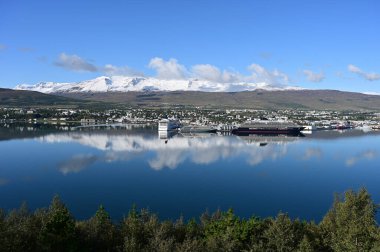 Akureyri, İzlanda - 9 Eylül 2023 - Akureyri ve çevresindeki manzara berrak güneşli bir sonbahar sabahı sakin sulara yansıdı.