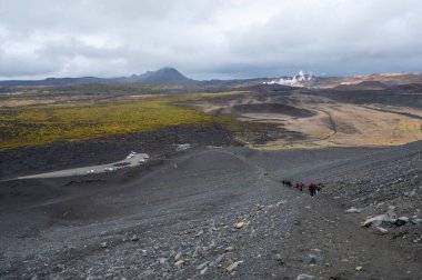 Myvatn, İzlanda 'nın doğusundaki Hverfjall kraterinin kenarına giden yürüyüşçüler sonbahar öğleden sonraları arka planda jeotermal alan ile bulutlu hava manzarası oluşturuyorlar...