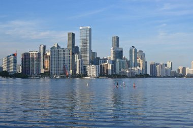 Miami, Florida - 12-27-2023 - Standup paddleboardcuları ve şehir silueti güneşli Aralık akşamında Biscayne Körfezi 'nin sakin sularına yansıdı.