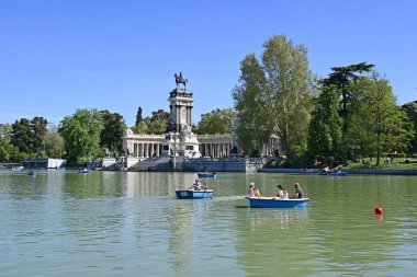 Madrid, İspanya - 13 Nisan 2024 - Aileler güneşli Cumartesi sabahı Retiro Park 'taki Büyük Havza' da Alfonso XII anıtı arka planında kürek çekmenin keyfini çıkarıyorlar.