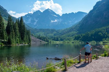 Ziyaretçiler, dramatik yaz bulutları altında güneşli bir yaz öğleden sonrasında Maroon Bells ve Lake manzarasının keyfini çıkarıyorlar...