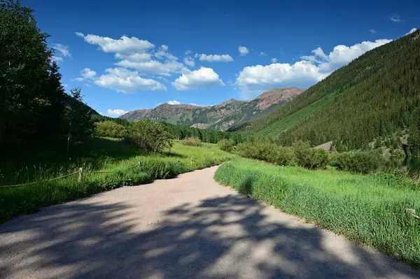 Stock image Walking trail around Maroon Lake with view of Maroon Bells on sunny afternoon under dramatic summer cloudscape.