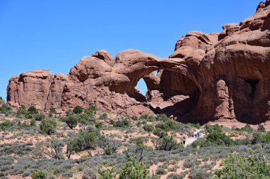 Distant tourists on Double Arch trail in Arches National Park near Moab, Utah on clear sunny summer morning. clipart