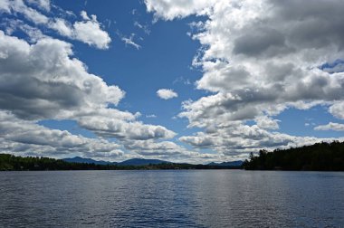 Güneşli bir öğleden sonra New York, Placid Gölü üzerinde açık yaz bulutları ve arka planda Adirondack Dağları.