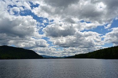 Güneşli bir öğleden sonra New York, Placid Gölü üzerinde açık yaz bulutları ve arka planda Adirondack Dağları.