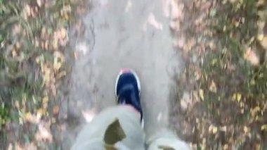 Bir adam toprak bir yolda spor ayakkabılarla yürüyor.