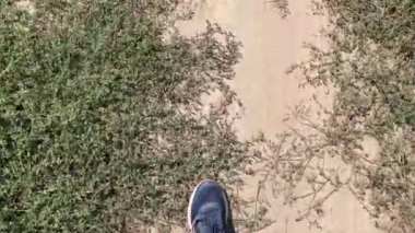 Bir adam toprak bir yolda spor ayakkabılarla yürüyor.