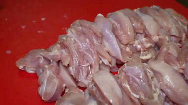 Mutfak hassasiyeti, tavuk doğrayıcı fileto. Eldivenli bir el kırmızı bir kesme tahtasındaki bıçağı ustalıkla kullanır, bir tavuk filetosunu pişirmeye hazır, küçük, üniformalı küplere dönüştürür.