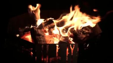 Geceyi ateşleyen şenlik ateşi. Küçük bir şenlik ateşi, odun parçalarının üzerinde dans eden alevler, altın parıltılarıyla çevreyi aydınlatıyor..