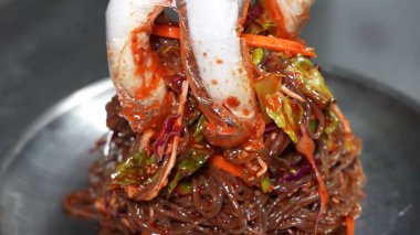 Bir tabak taze soba eriştesi, otlar, sebzeler, susam tohumları ve parlak bir sosla süslenmiş..